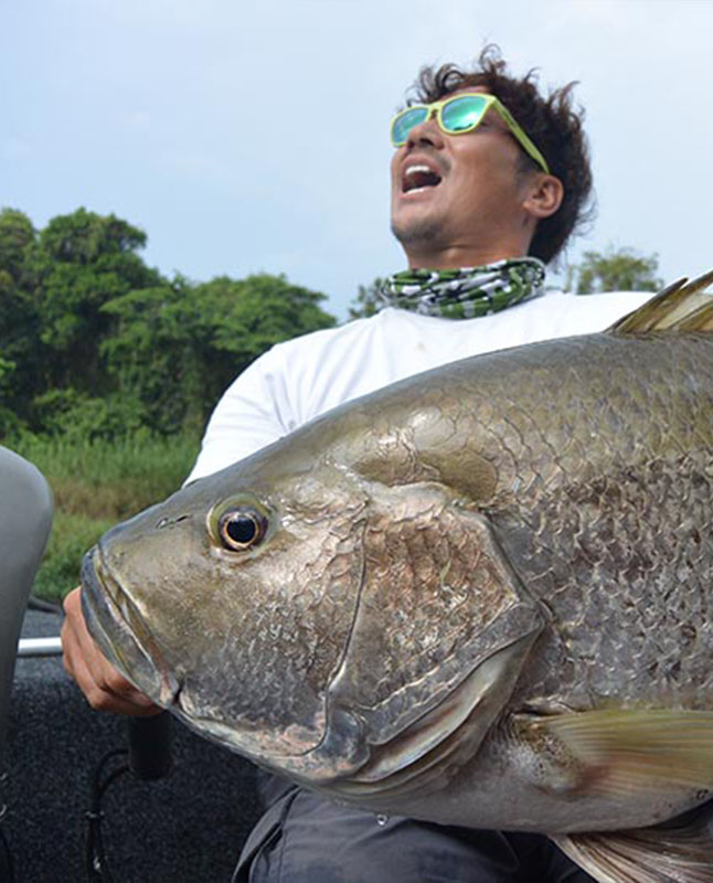 A man with a smile on his face holding a large fish in a boat.