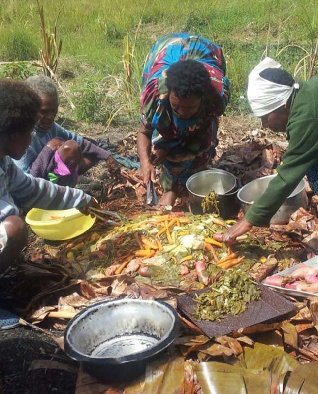 A group of individuals cooking a meal together on the ground.