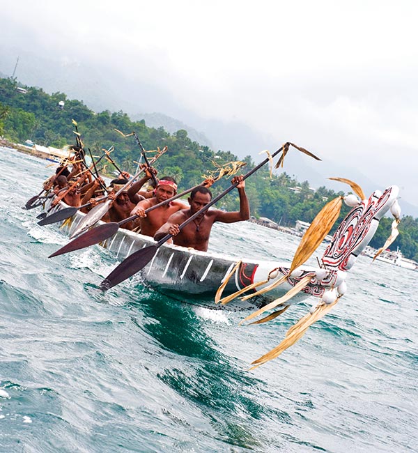 A group of men paddling in a canoe while in the ocean.